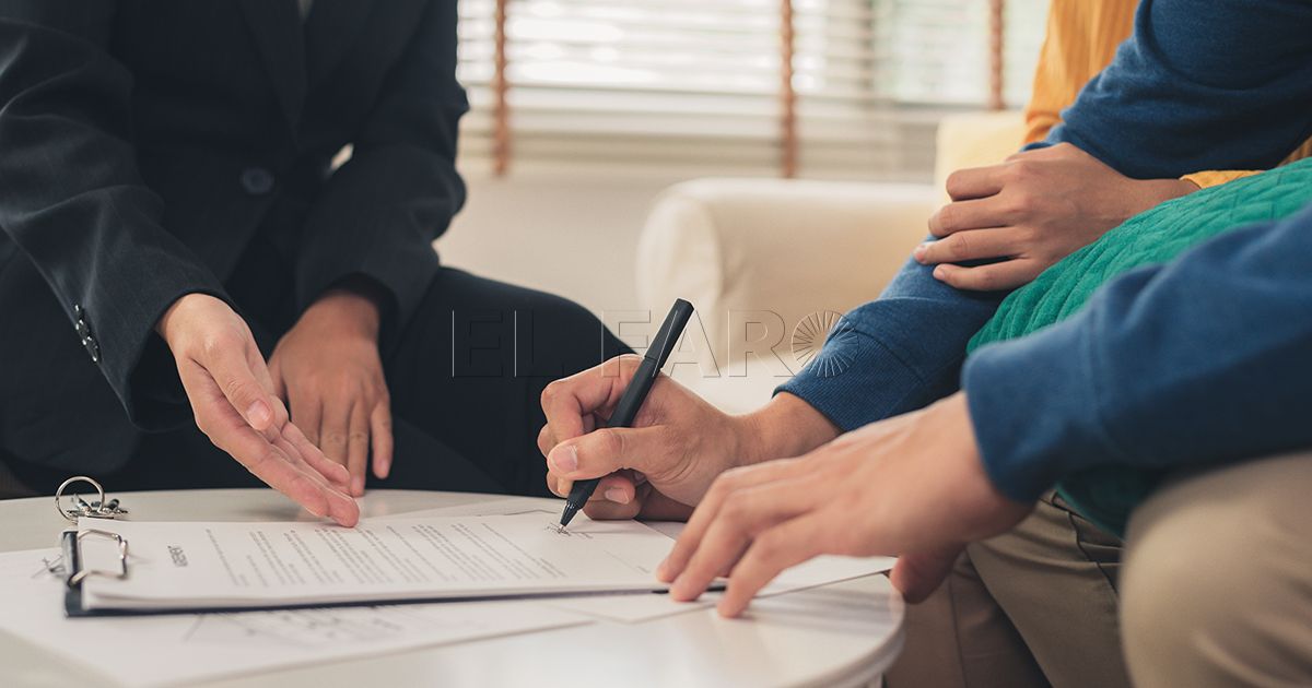 Happy young Asian couple and realtor agent. Cheerful young man signing some documents while sitting at desk together with his wife. Buying new house real estate. Signing good condition contract.