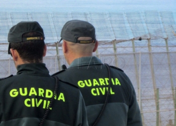 GRA295. MELILLA, 03/04/2014.- Agentes de la Guardia Civil ante los inmigrantes de origen subsahariano que permanecen en lo alto de la valla de Melilla, tras casi 10 horas encaramados a una altura de seis metros, después de protagonizar junto a otros 150 subsaharianos un intento de entrada masivo a Melilla. Dos de los inmigrantes se encuentran esta tarde en lo alto de la valla, mientras que el resto han comenzado a bajar con la ayuda de una escalera y, acompañados por agentes de la Guardia Civil. EFE/Noelia Ramos