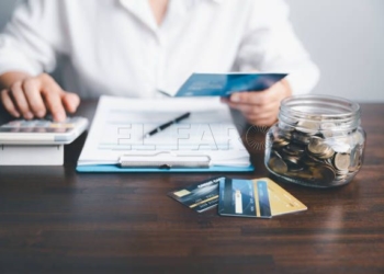 Business woman hands holding saving account passbook with calculator, account and saving concept. Asian woman checking bills, taxes, bank account balance and calculating credit card expenses.