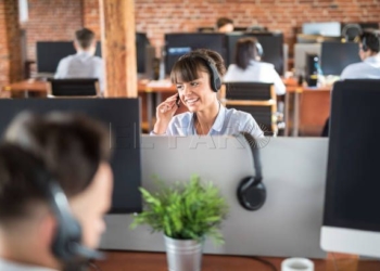 Call center worker accompanied by her team. Smiling customer support operator at work. Young employee working with a headset.